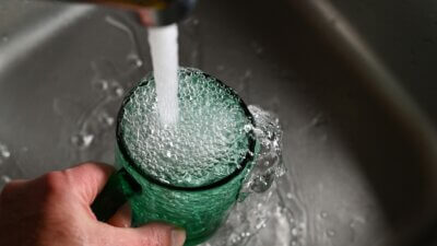 Voda teče iz slavine u čašu u sudoperu.
