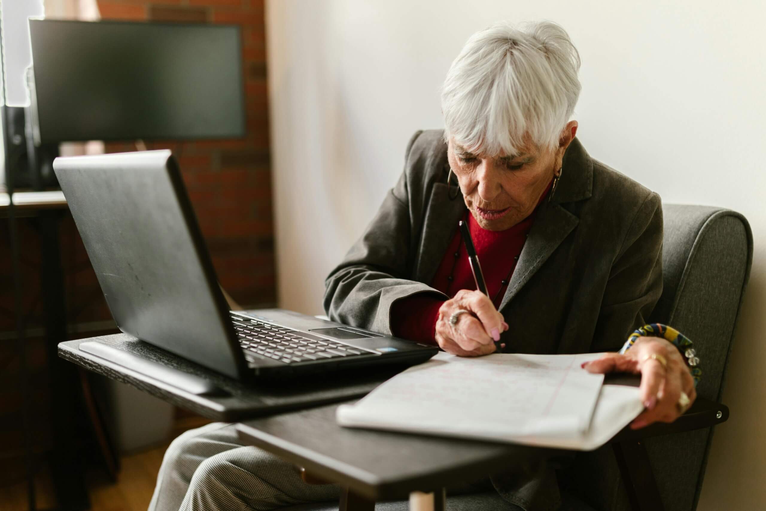 Starija ženska osoba sjedi za stolom uz laptop i papire
