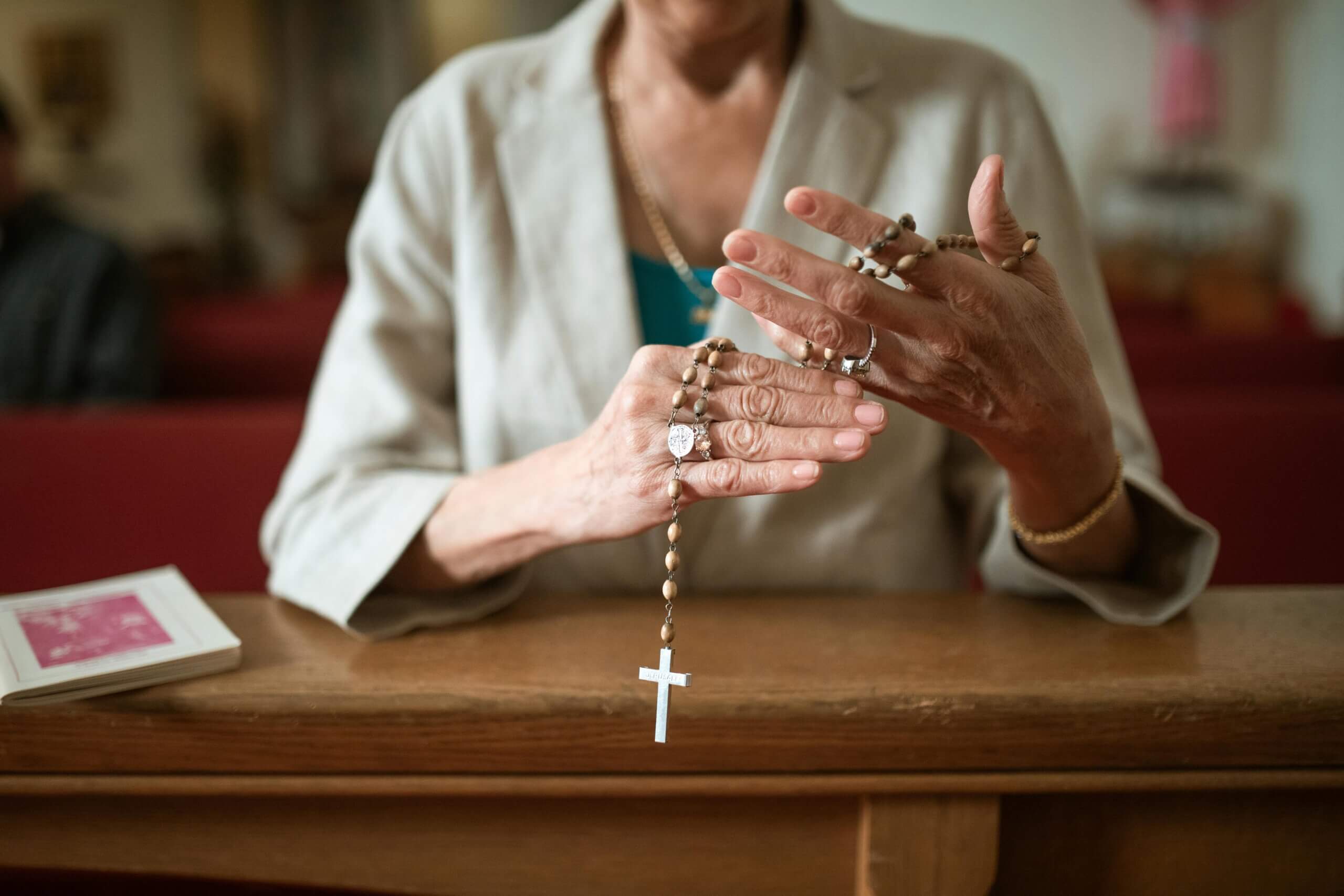 Starija ženska osoba u crkvi u rukama drži krunicu